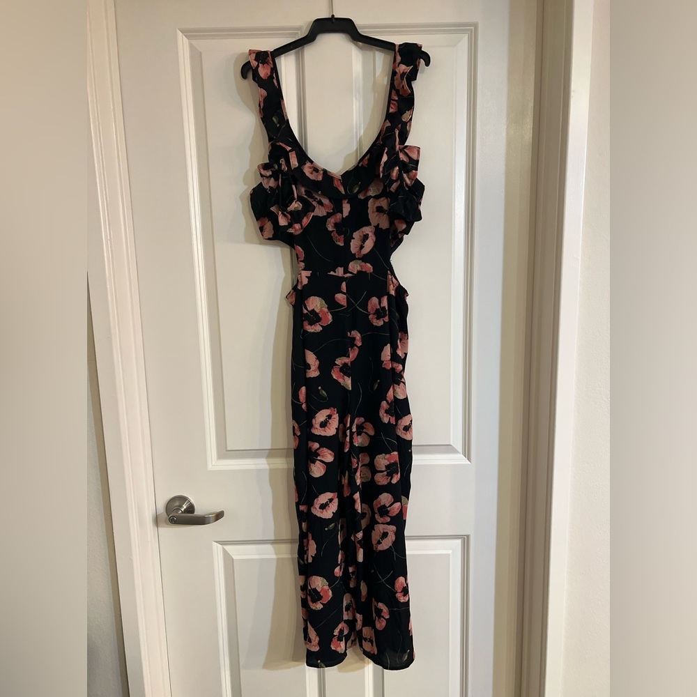 Black wide leg jumpsuit with floral pattern. Side cut out with ruffled staps